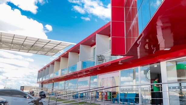 A modern building with a red and white facade, large windows, and a covered outdoor area.