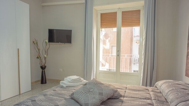A bedroom with a bed, a TV, a window with blinds, and a plant. - Apartment Enea Centralissimo Rinnovato, Vicinissimo Alla Stazione e Attrazioni (Pompei)