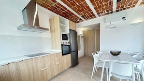 A modern kitchen with wooden cabinets, a built-in oven, and a dining area with white chairs and a table. - Agi Arago 271 Apartamento for rent in Roses Girona. (Roses)