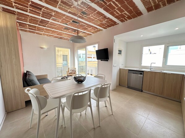 A modern kitchen with a dishwasher, a dining area with a table and chairs, and a TV mounted on the wall.