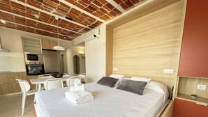 A modern bedroom with a large bed, a wooden headboard, a dining area with a table and chairs, and a kitchenette with a microwave and oven. - Agi Arago 273 Apartamento for rent in Roses Girona. (Roses)
