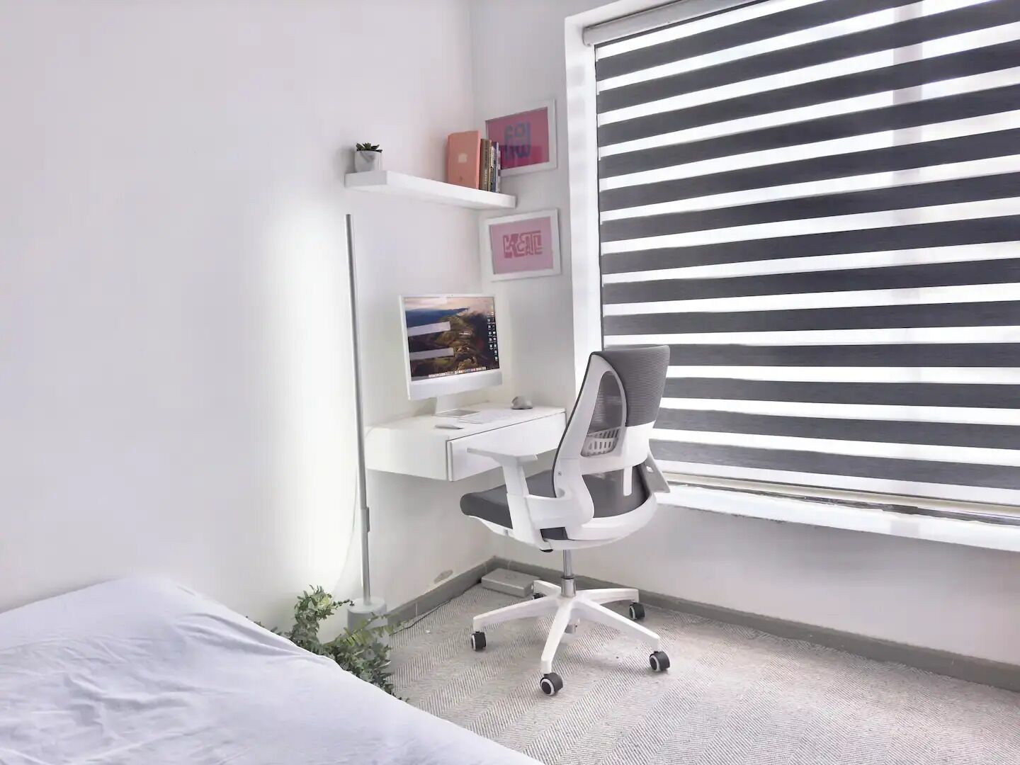 A neatly organized bedroom with a bed, a desk with a computer, and a window with blinds.
