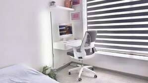 Une chambre bien rangée, avec un lit, un bureau équipé d’un ordinateur et une fenêtre avec des stores.