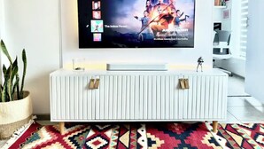Un salon moderne avec un téléviseur à écran plat fixé au mur, une console blanche et un tapis coloré.