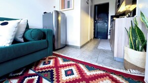 Un salon moderne avec un canapé de couleur turquoise, un tapis à motifs et un réfrigérateur.