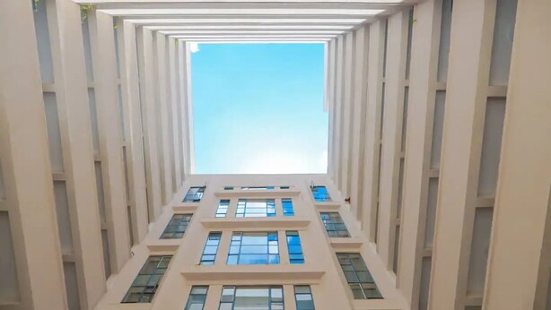 Un couloir doté d’un plafond haut et de nombreuses fenêtres de part et d’autre, qui donne sur un ciel lumineux.
