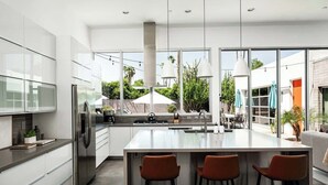 Une cuisine moderne dotée d’un grand îlot central, d’appareils électroménagers en acier inoxydable et offrant une vue sur l’extérieur.