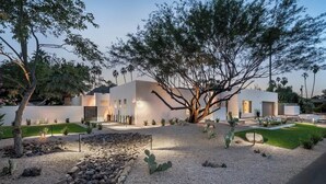 Une maison moderne à l’extérieur blanc, entourée d’un jardin aménagé avec des cactus et des arbres.