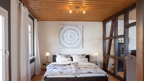 Een slaapkamer met een groot bed, twee nachtkastjes met lampen, een houten plafond en een groot raam met uitzicht.