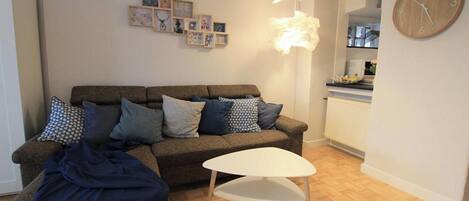 A living room with a brown sofa, patterned cushions, a white coffee table, and a wall clock.