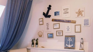 A room with a wooden chair, a white radiator, and nautical-themed wall decor including framed pictures and a starfish.