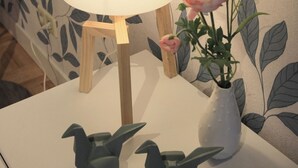 A bedside table with a lamp, a vase with a flower, and two bird-shaped objects.