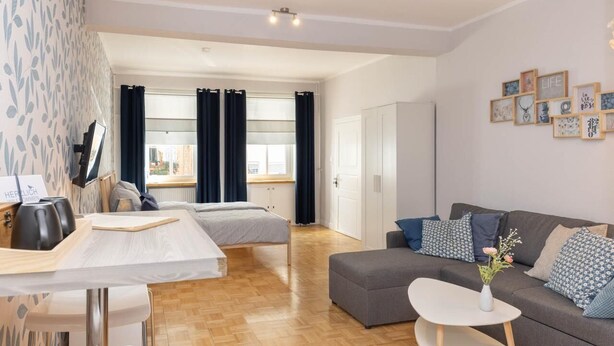 A modern hotel room with a wooden floor, a sofa, a dining table, and a TV. - RankenNest (Bad Ems)