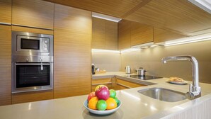 A modern kitchen with wooden cabinets, stainless steel appliances, a bowl of fruit on the counter, and a sink with a faucet. - Aspasios Diagonal Art (Barcelona)