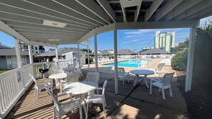 Uma área externa coberta com piscina, cadeiras e mesas de plástico branco.