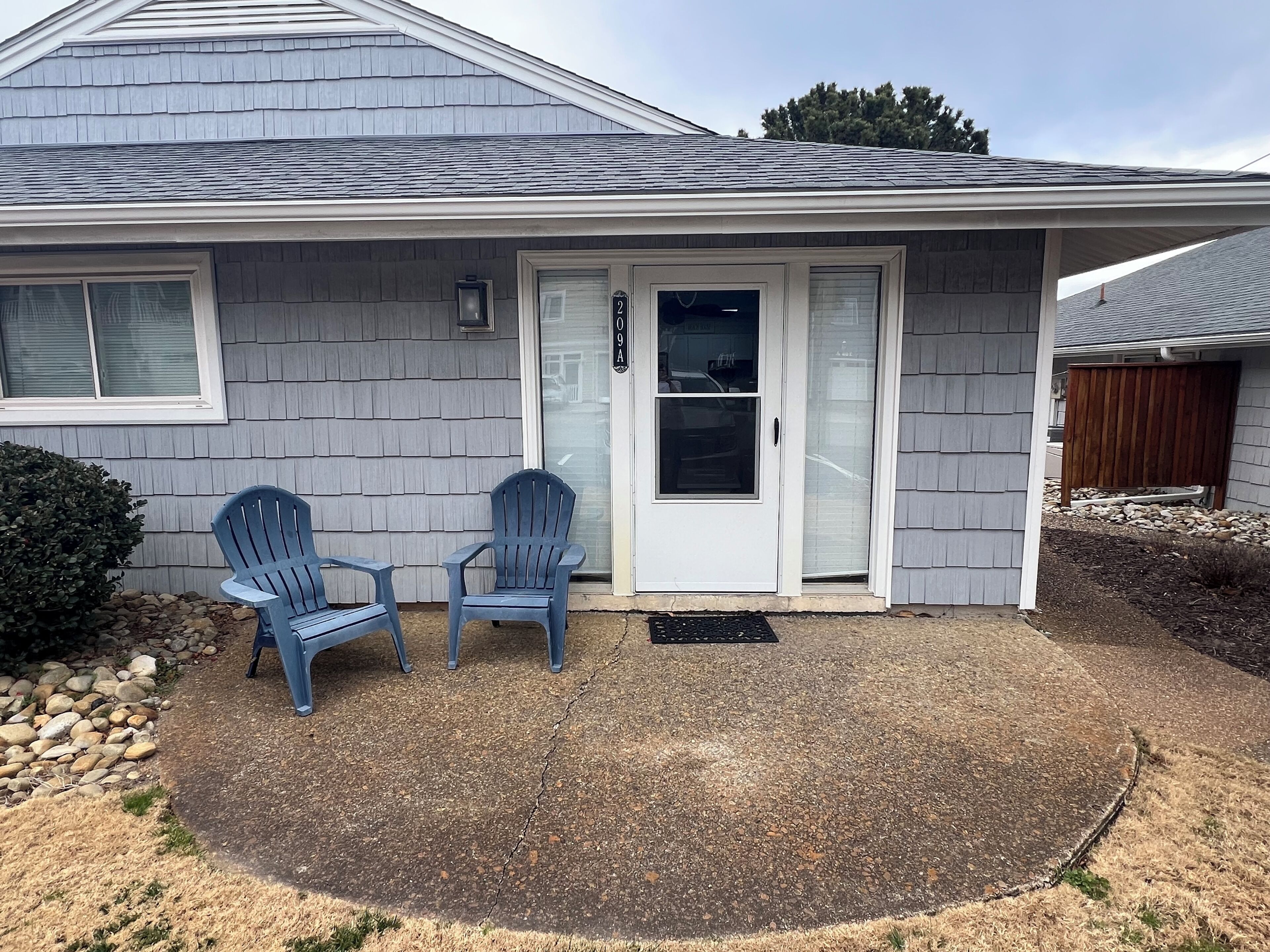A house with a grey shingled roof, a white door, and two blue Adirondack chairs in the front yard.
