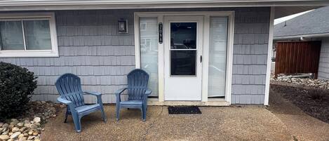 A house with a grey shingled roof, a white door, and two blue Adirondack chairs in the front yard.