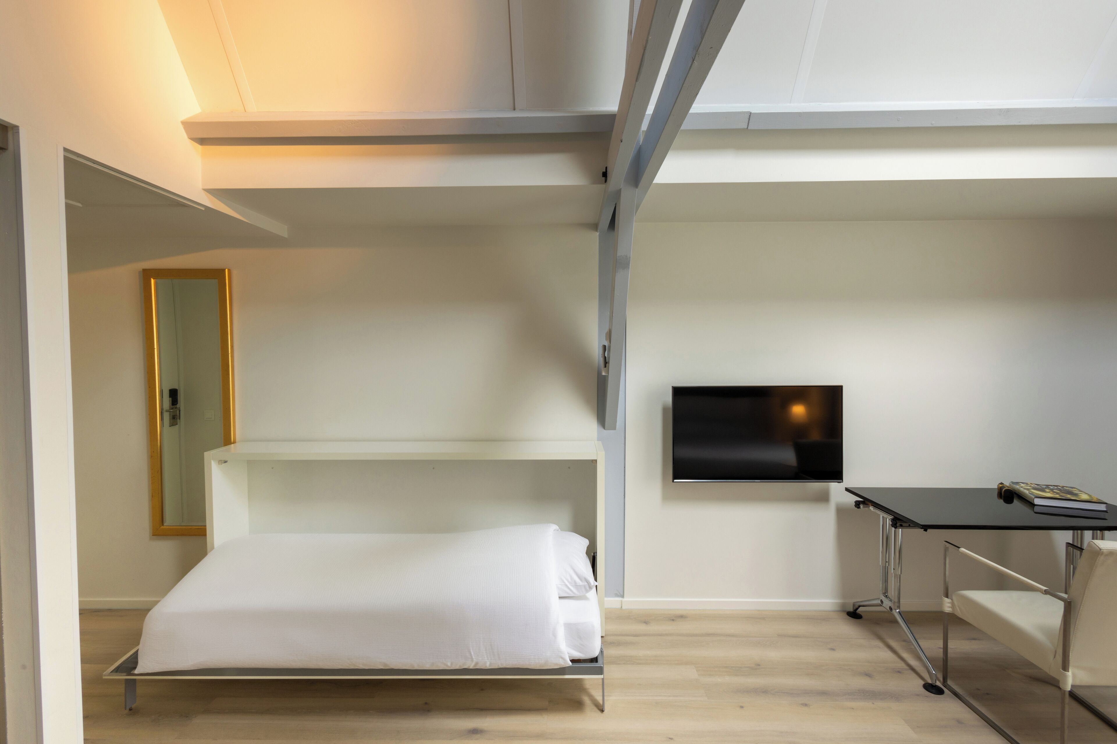 Una habitación de hotel moderna con cama, escritorio, silla, televisor y espejo.