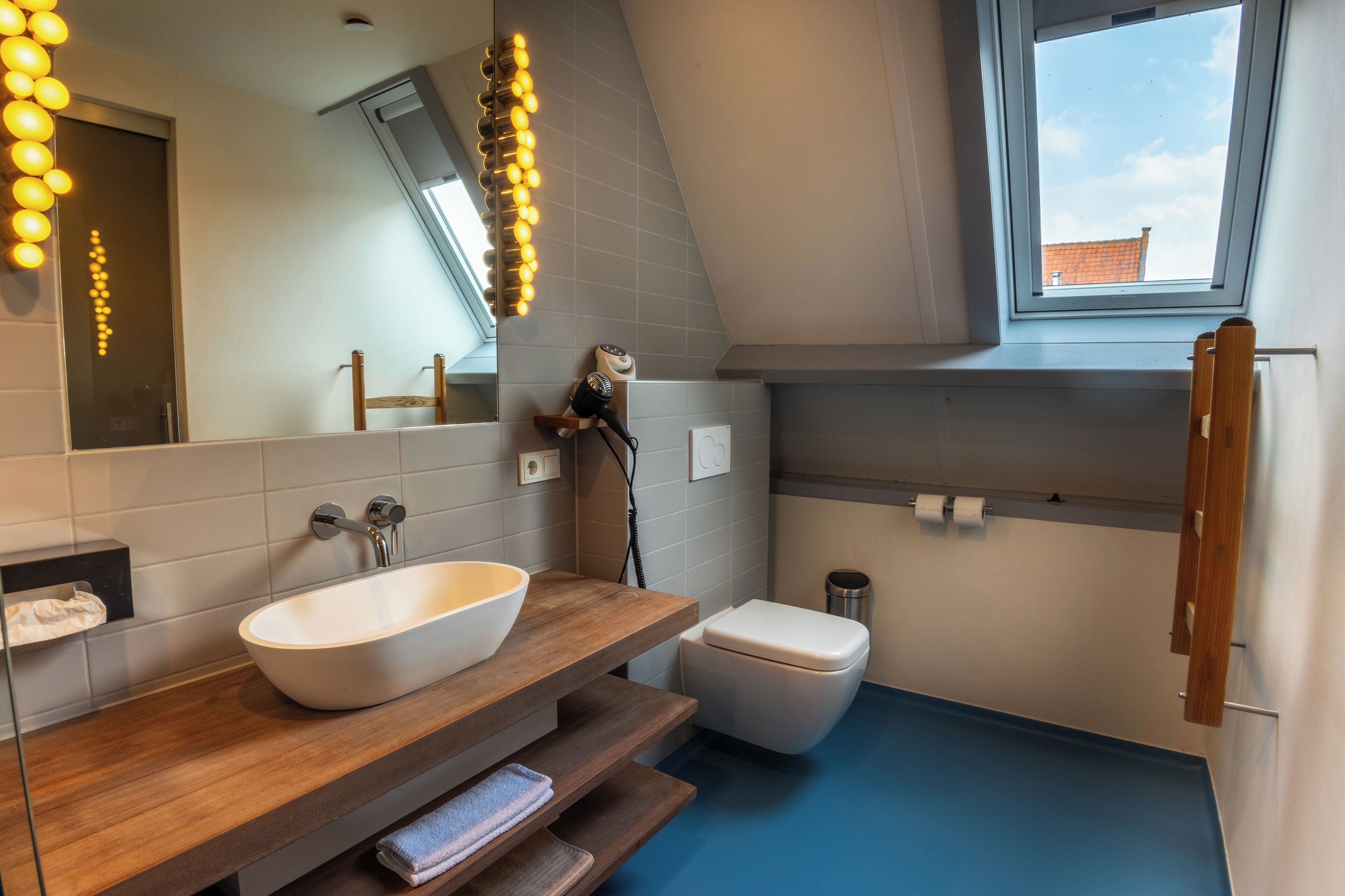 A modern bathroom with a wooden vanity, a large mirror, and a skylight.