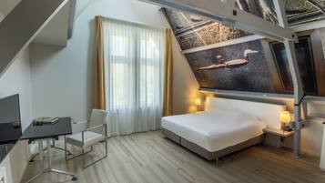 A modern hotel room with a bed, desk, chair, and a large mural on the ceiling.