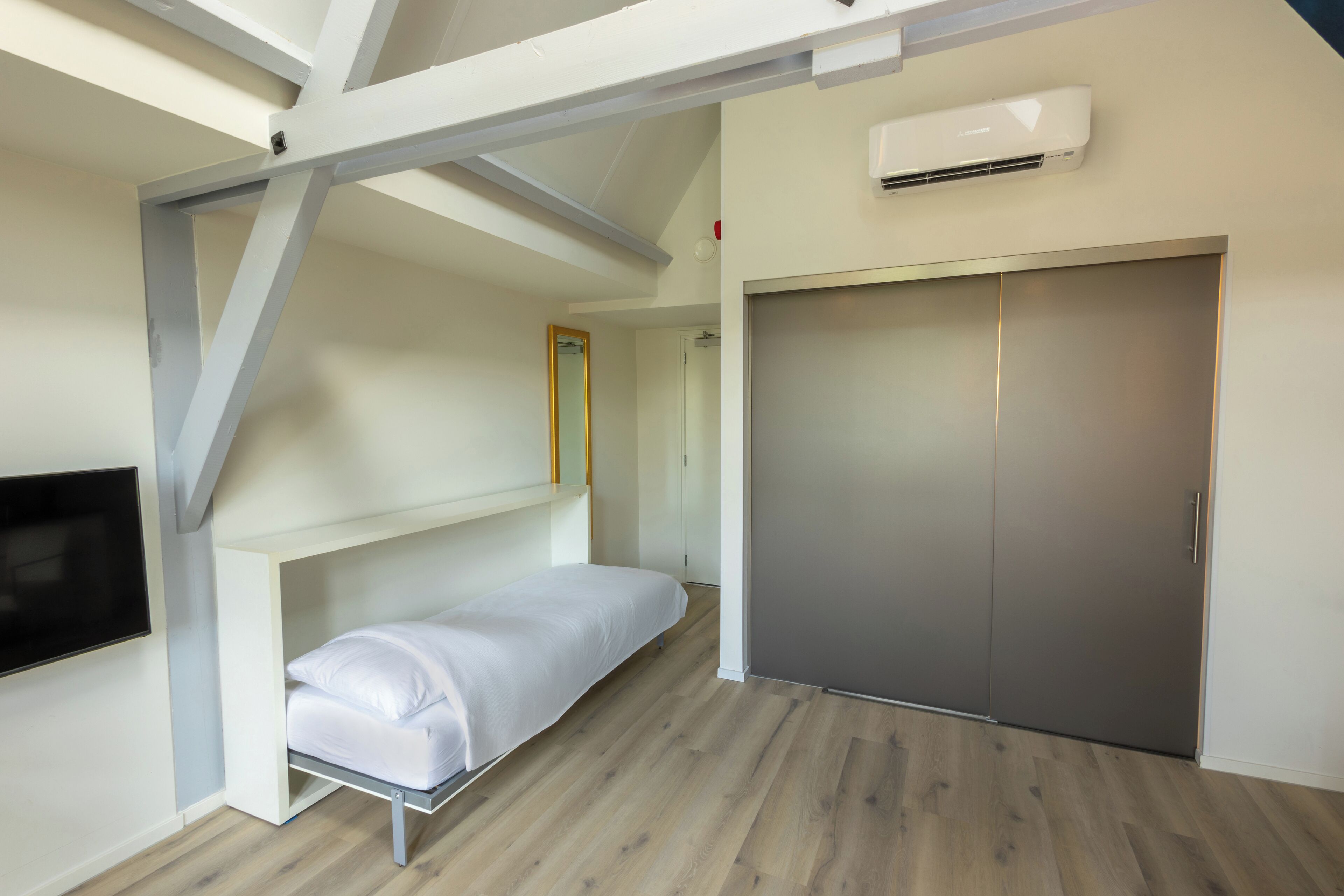 A modern bedroom with a bed, a wardrobe, and a mounted TV.