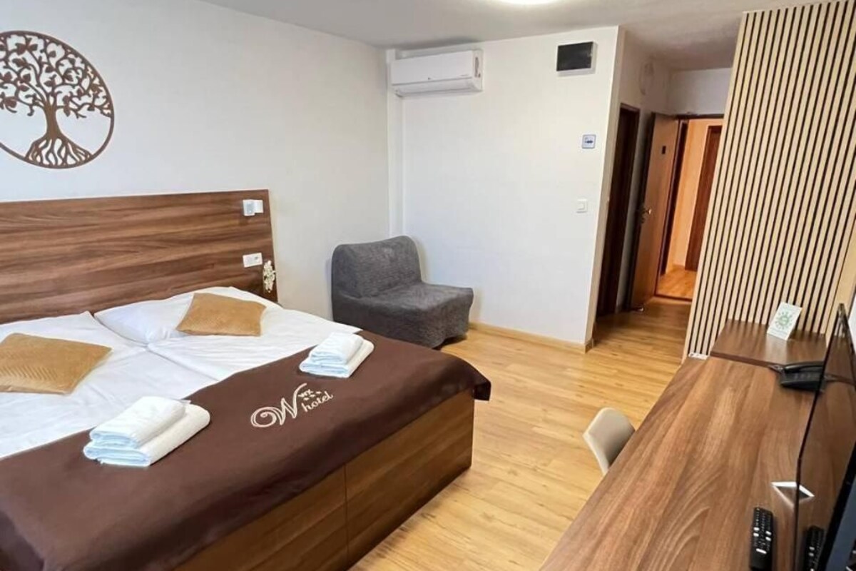 Habitación de hotel con cama, escritorio, silla, sillón gris y decoración en la pared.