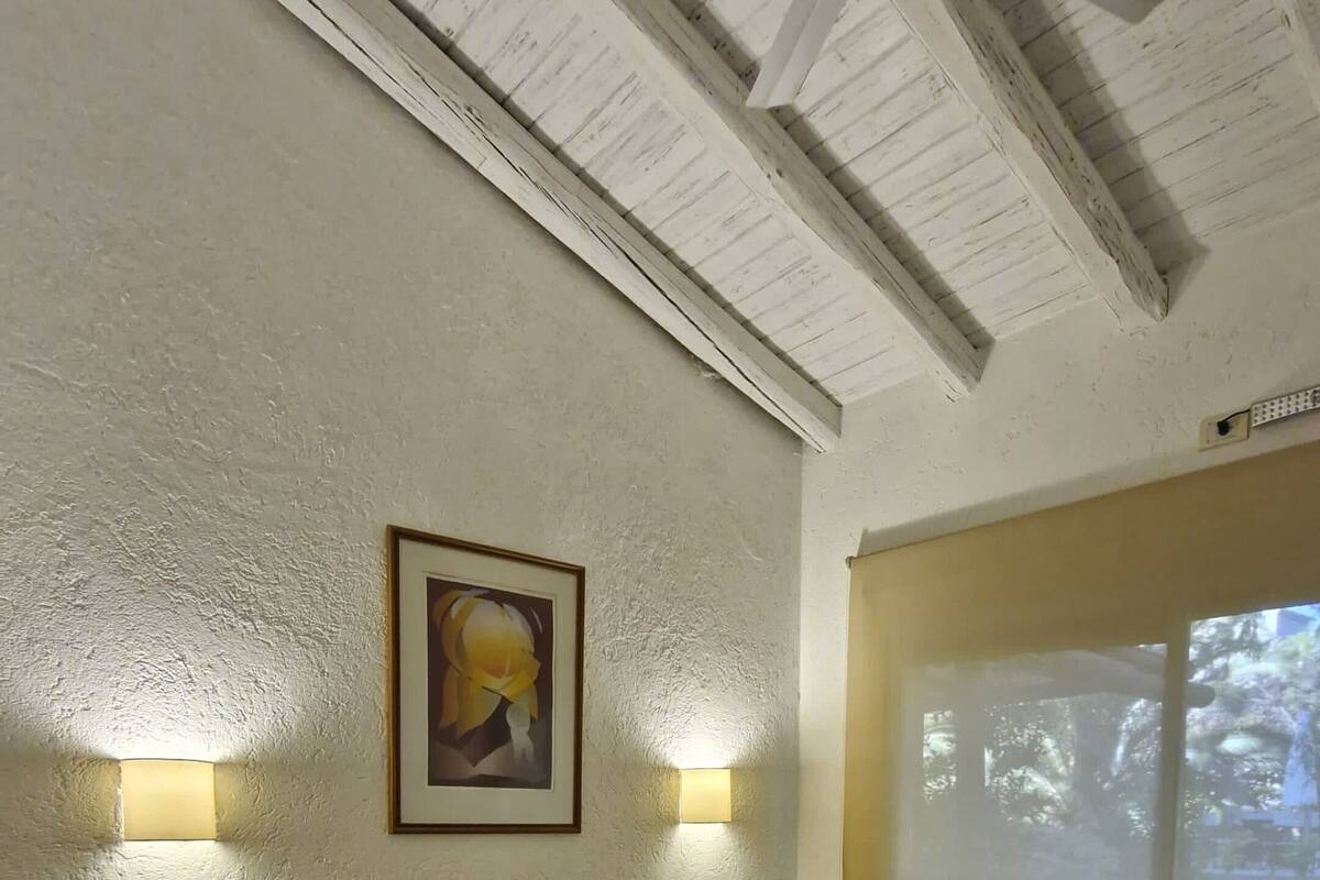Una habitación con dos camas, un ventilador de techo, un cuadro enmarcado y una ventana con vista a árboles.