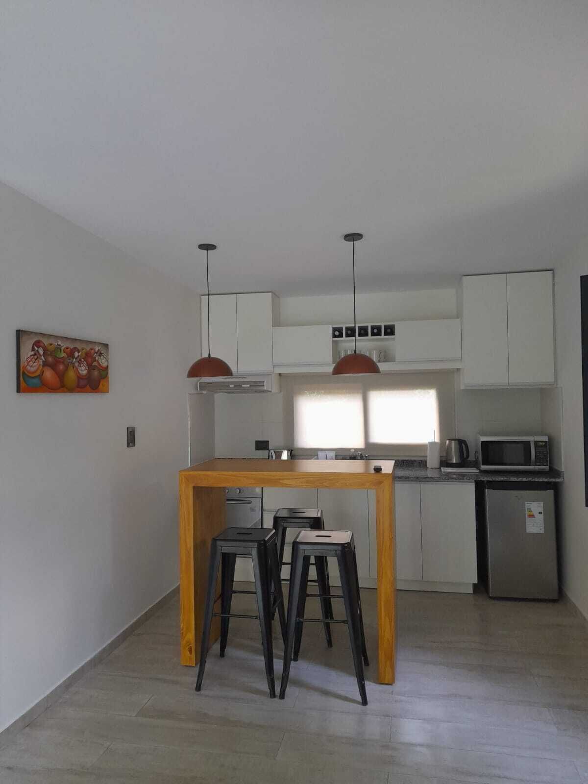 A modern kitchen with white cabinets, a wooden island, two bar stools, and pendant lights.