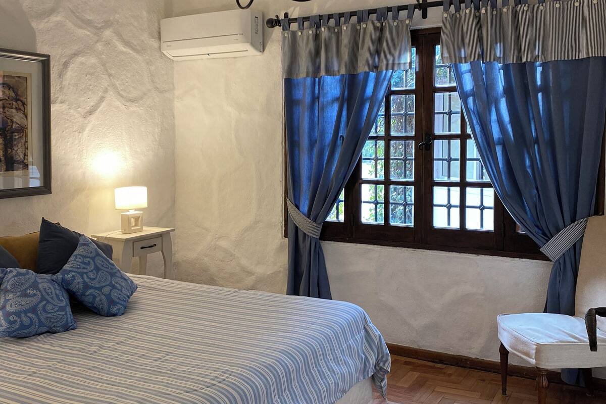 Un dormitorio con una cama, una silla, una ventana con cortinas, una lámpara y una lámpara del techo.