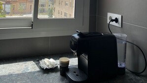 Una habitación con ventana que da a un paisaje urbano, una cafetera y una taza de café sobre la encimera.