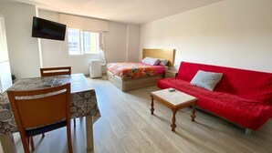 Una habitación compacta con cama, un sofá rojo, una mesa de comedor con sillas y un televisor de pantalla plana montado en la pared.
