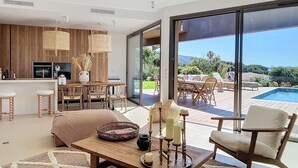 Una cocina moderna con armarios de madera, un comedor con mesa y sillas, y un amplio ventanal corredera que da a una terraza exterior con piscina.