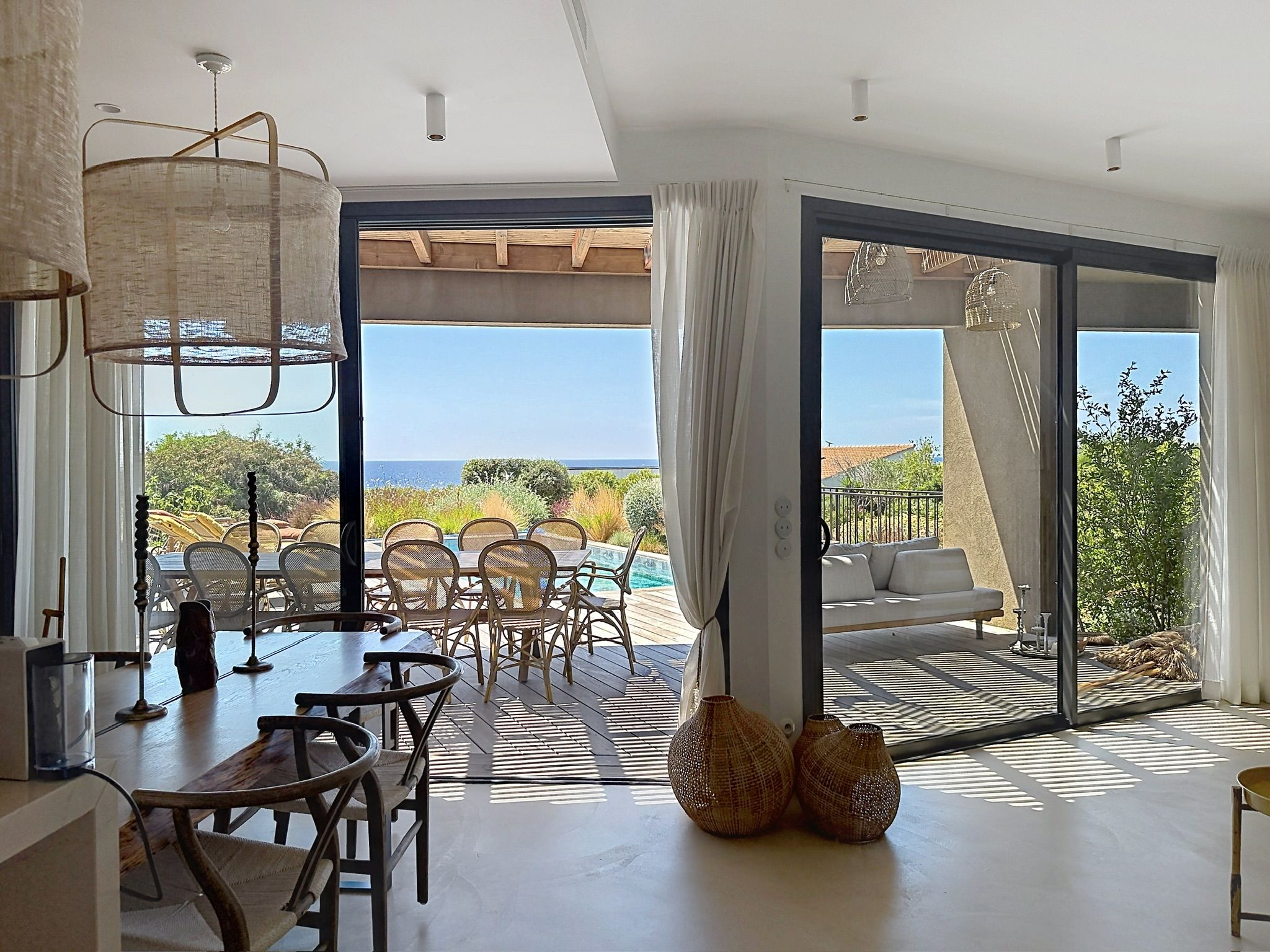 A modern interior with a dining area, a sofa, and a view of the outdoors.