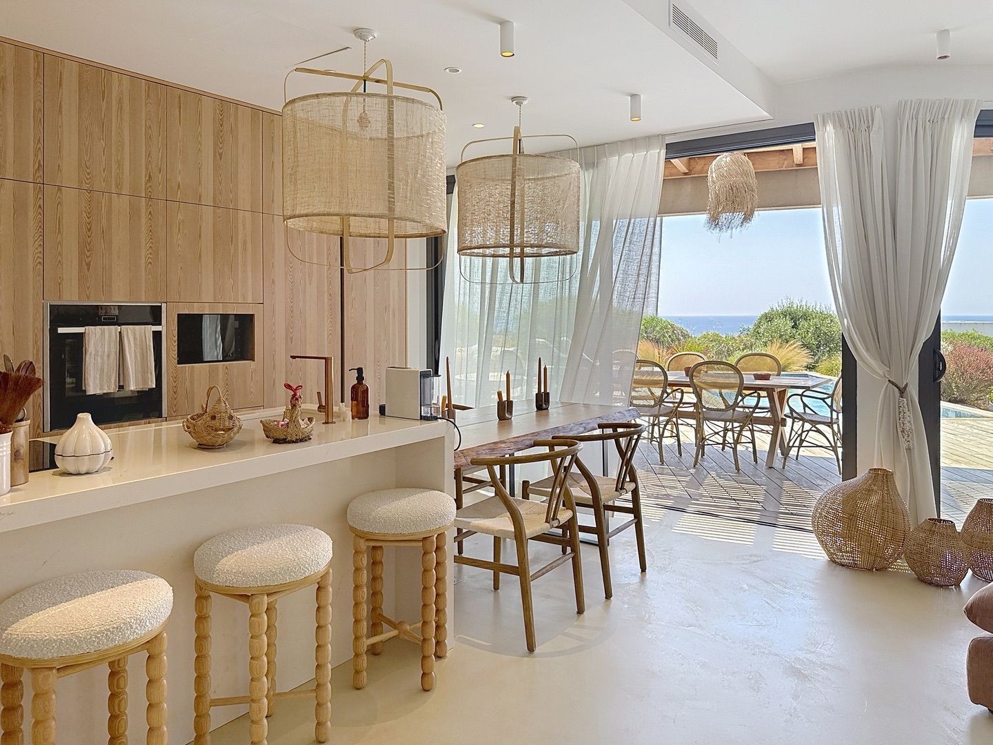A modern kitchen with a bar area, wooden stools, and a view of the sea.