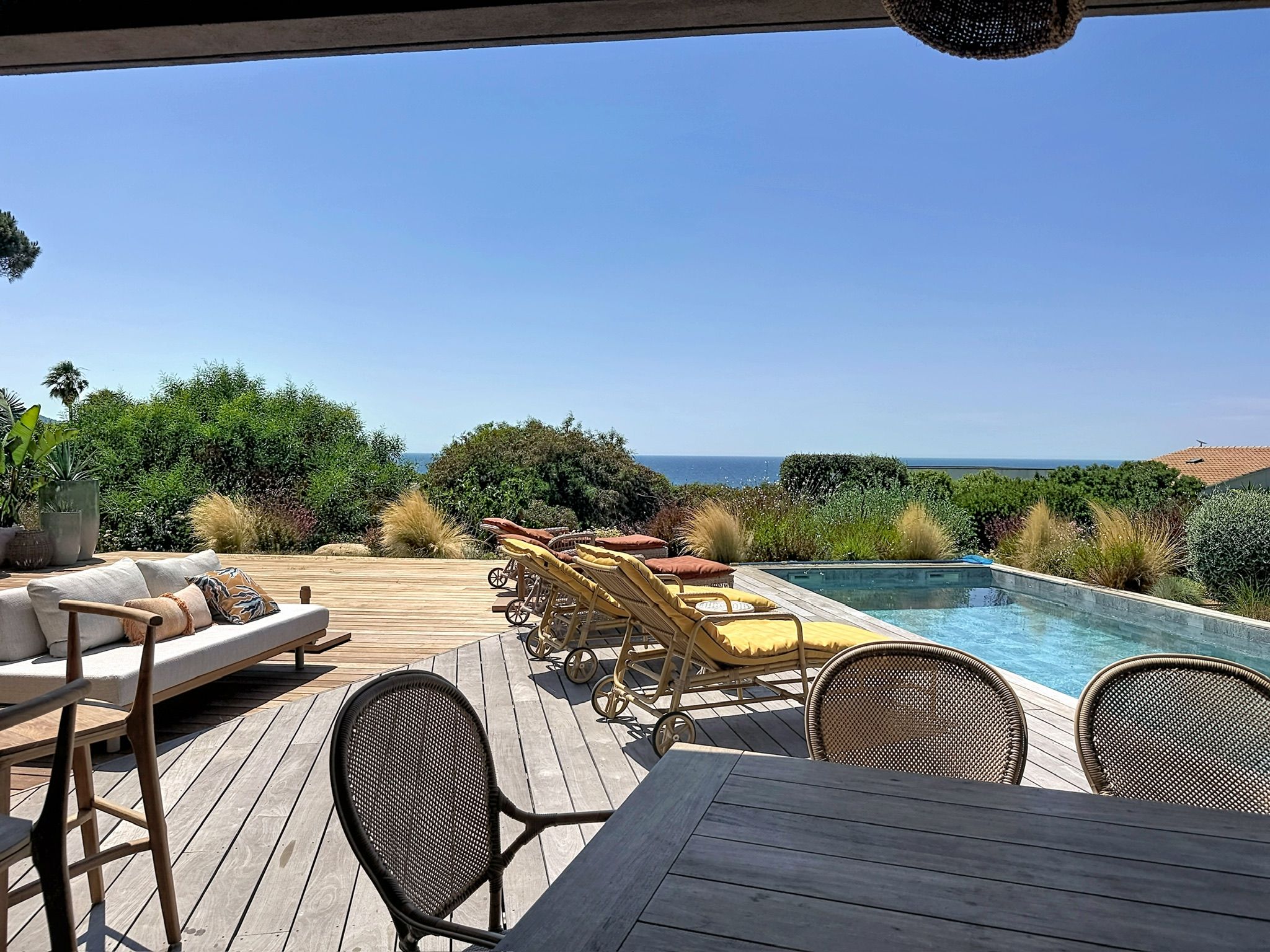 A wooden deck with outdoor furniture, a pool, and a view of the ocean.
