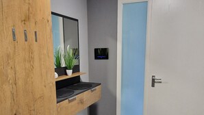 A room with a wooden wardrobe, a small shelf with a plant, a mirror, a door with a blue panel, and a tiled floor. - Haus am Wald Quietly located vacation apartment on the ground floor with terrace (Bad Tabarz)