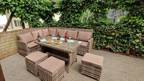 An outdoor seating area with wicker furniture and a table set for dining, surrounded by lush greenery. - Haus am Wald Quietly located vacation apartment on the ground floor with terrace (Bad Tabarz)