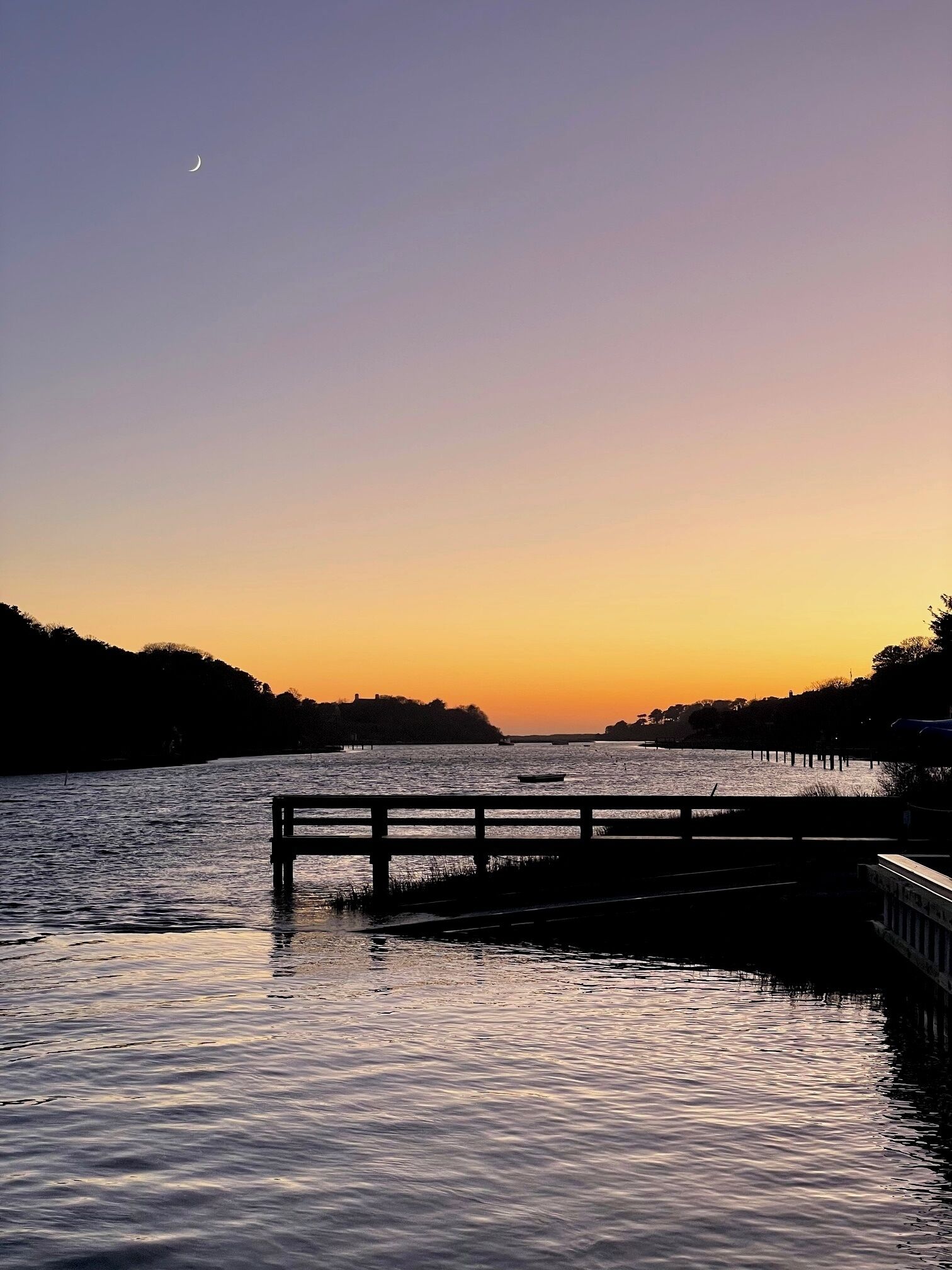A sunset over a calm body of water with a wooden dock and a small boat.