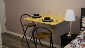 Ein Essbereich mit einem Tisch für zwei Personen, komplett mit Tellern, Besteck und Gläsern. Eine Lampe steht auf einem Nachttisch neben dem Bett.