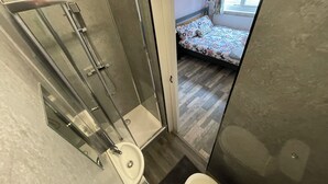 Ein modernes Badezimmer mit einer Glaskabine für die Dusche, einer Toilette und einem sichtbaren Schlafzimmer mit einem gemusterten Bettüberwurf.
