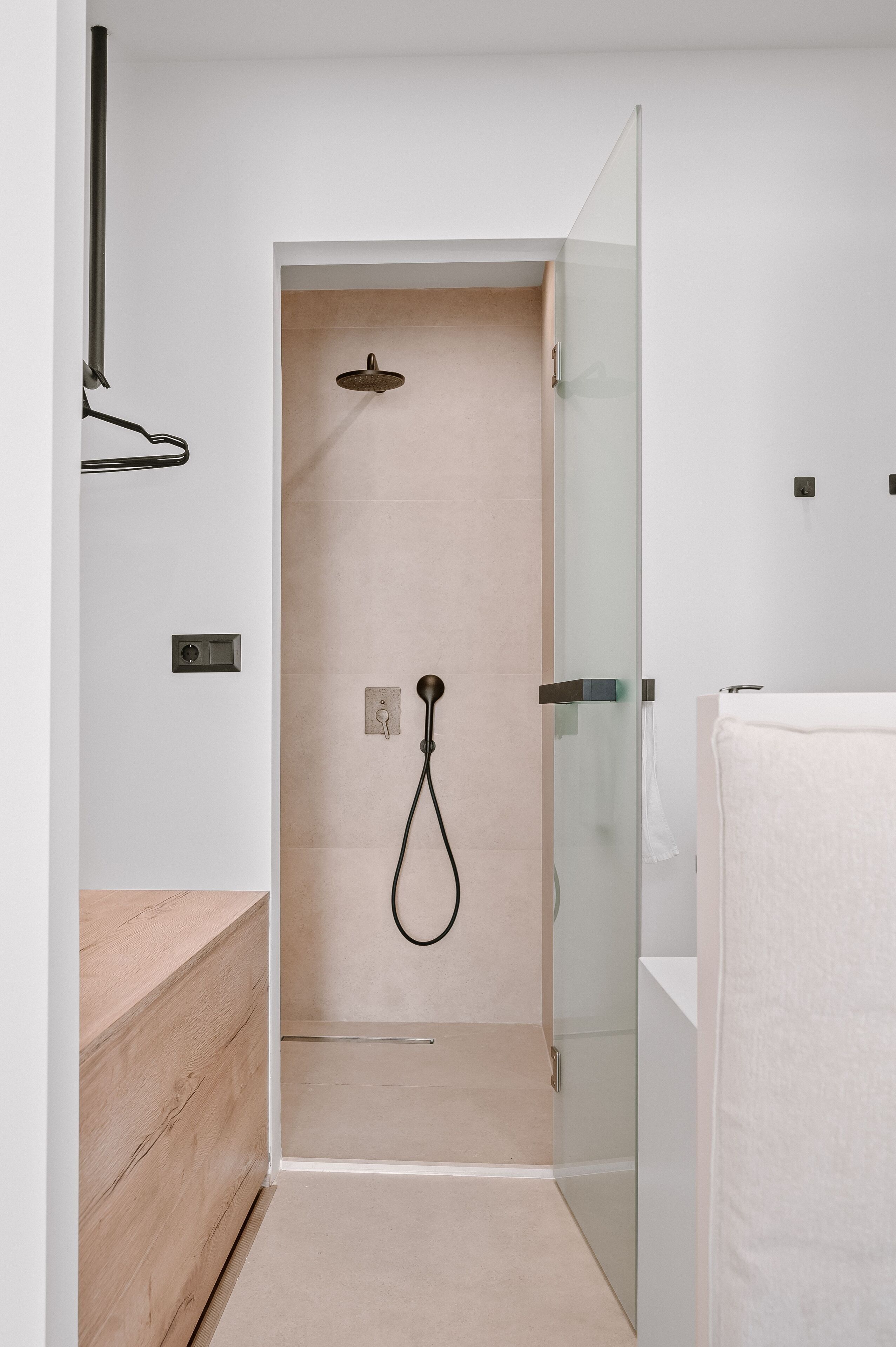 Ein modernes Badezimmer mit Duschkabine aus Glas, einem Holzausziehtisch und einem weißen Handtuch.