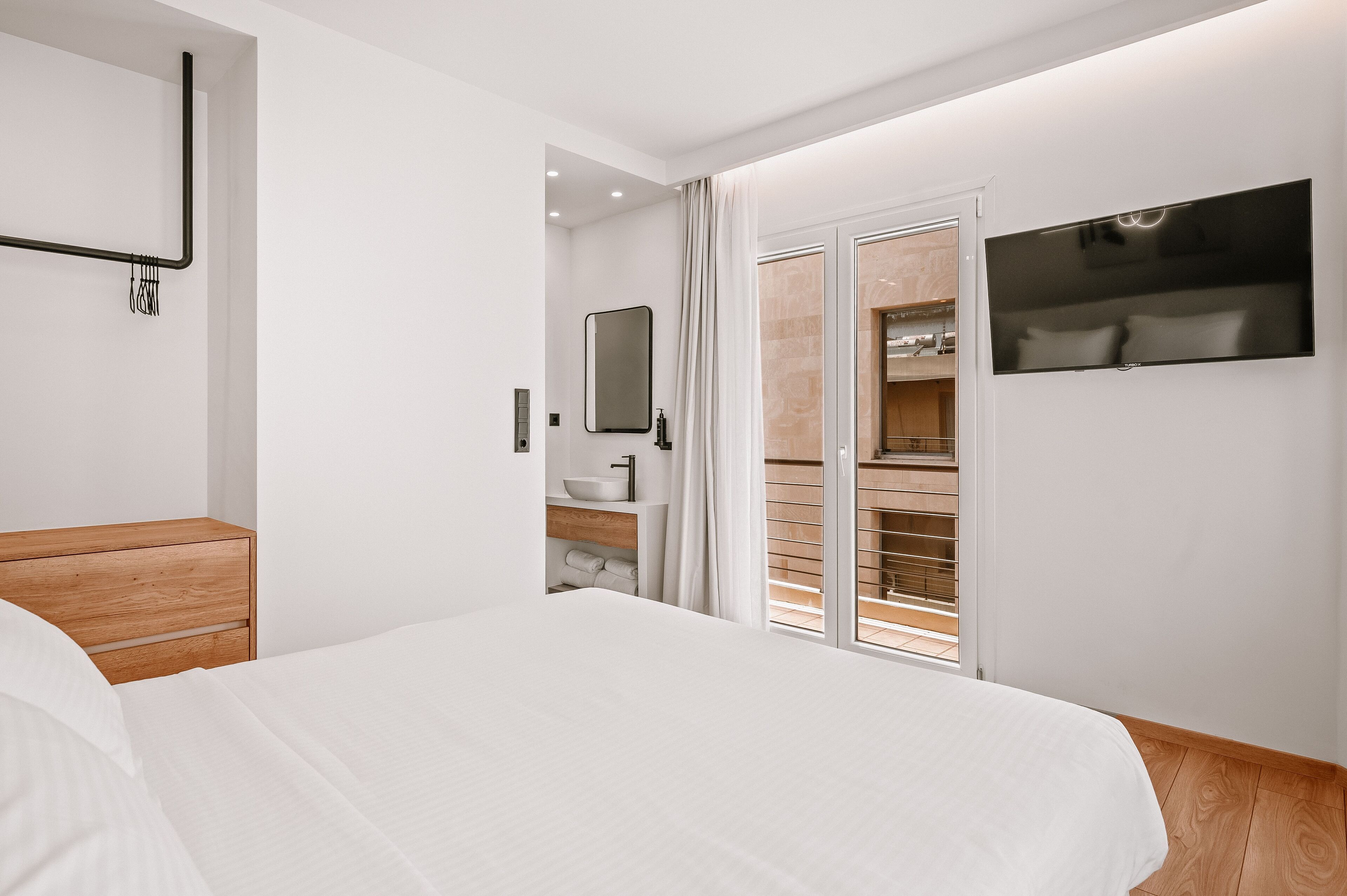 Quarto moderno com cama grande, mesa de cabeceira de madeira, armário embutido, espelho e televisão fixada na parede.