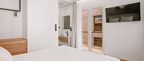 Quarto moderno com cama grande, mesa de cabeceira de madeira, armário embutido, espelho e televisão fixada na parede.