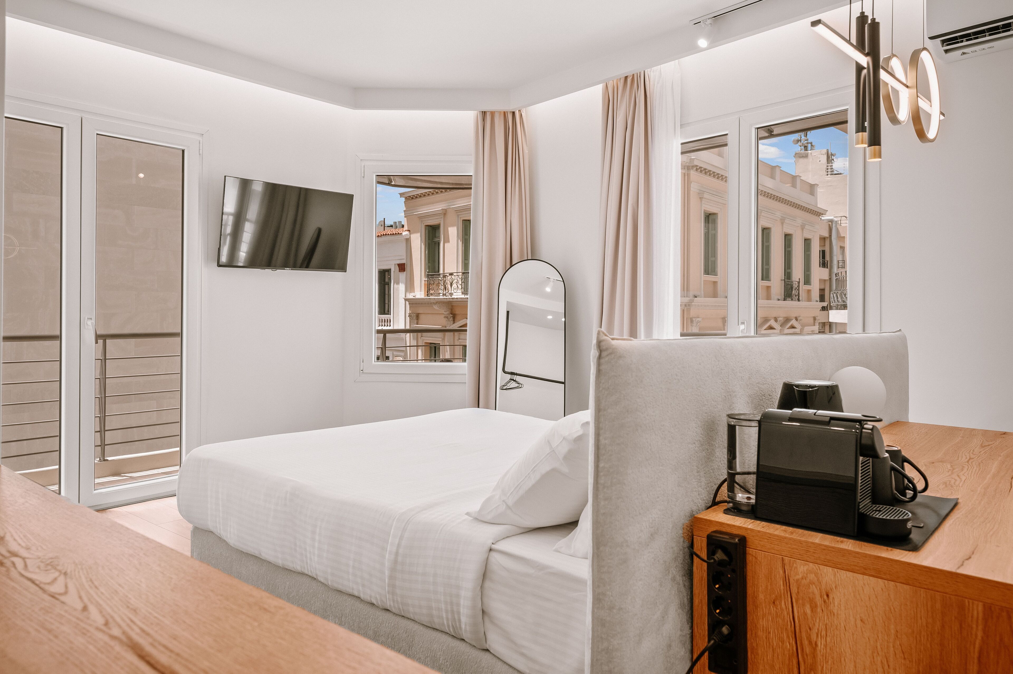 Habitación de hotel moderna con cama, escritorio con cafetera, televisión y vistas al balcón.