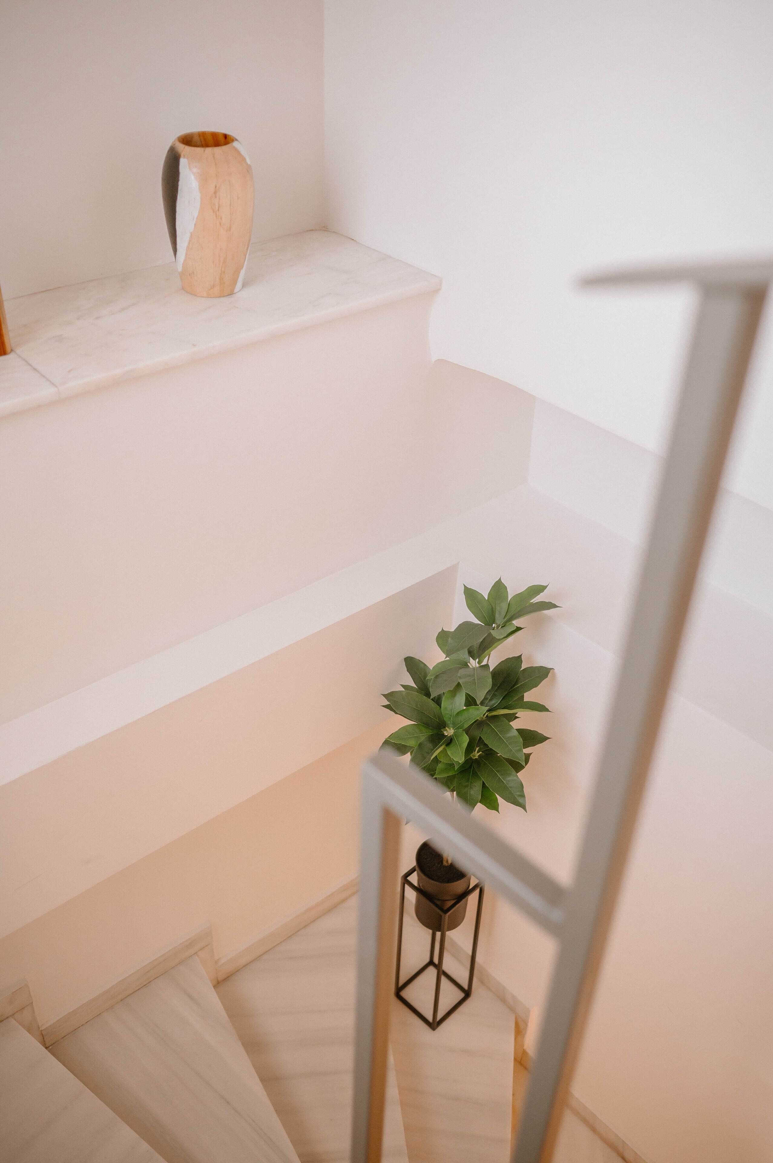Een trap met een witte muur, een houten vaas en een plant in pot op de overloop.