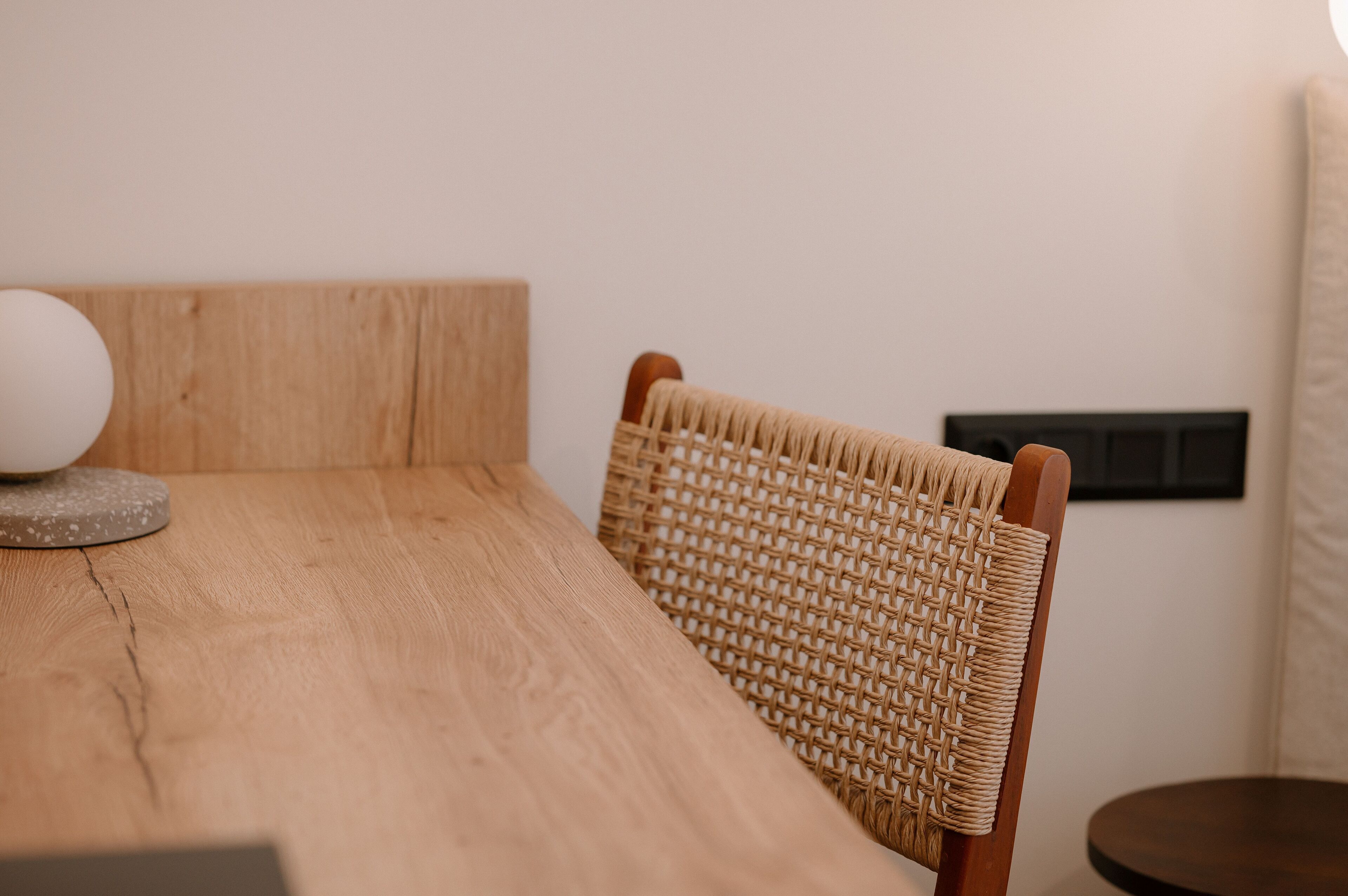 Una mesa de madera con una silla tejida y una mesa redonda al fondo.