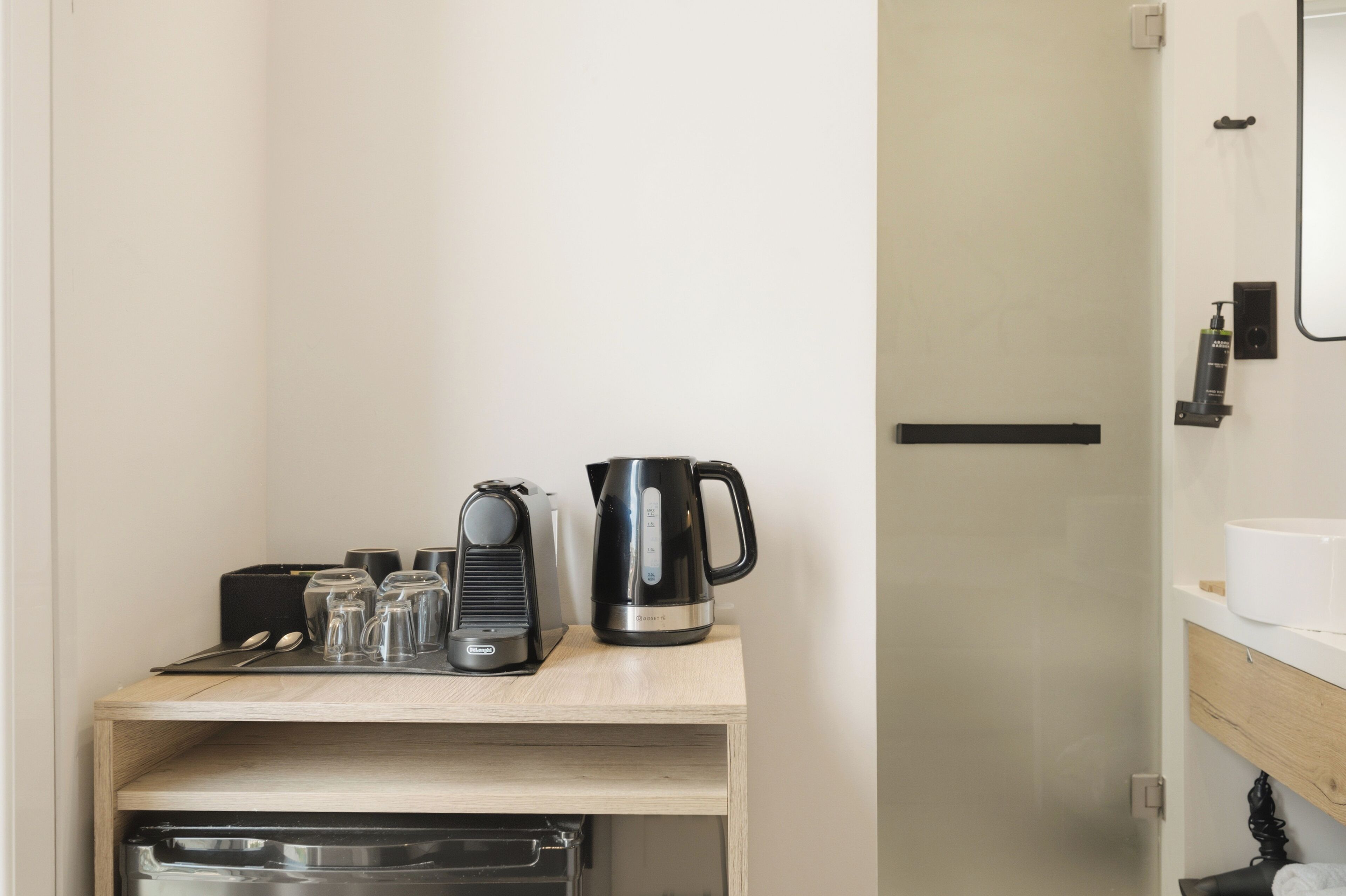 A small kitchenette with a coffee maker, a kettle, and a toaster on a wooden shelf.