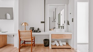 A modern bathroom with a white vanity, a mirror, a towel rack, and a wooden chair. - Plānis Str Urban Suites by Semavi (Heraklion)
