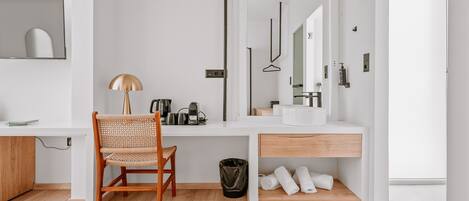 A modern bathroom with a white vanity, a mirror, a towel rack, and a wooden chair.