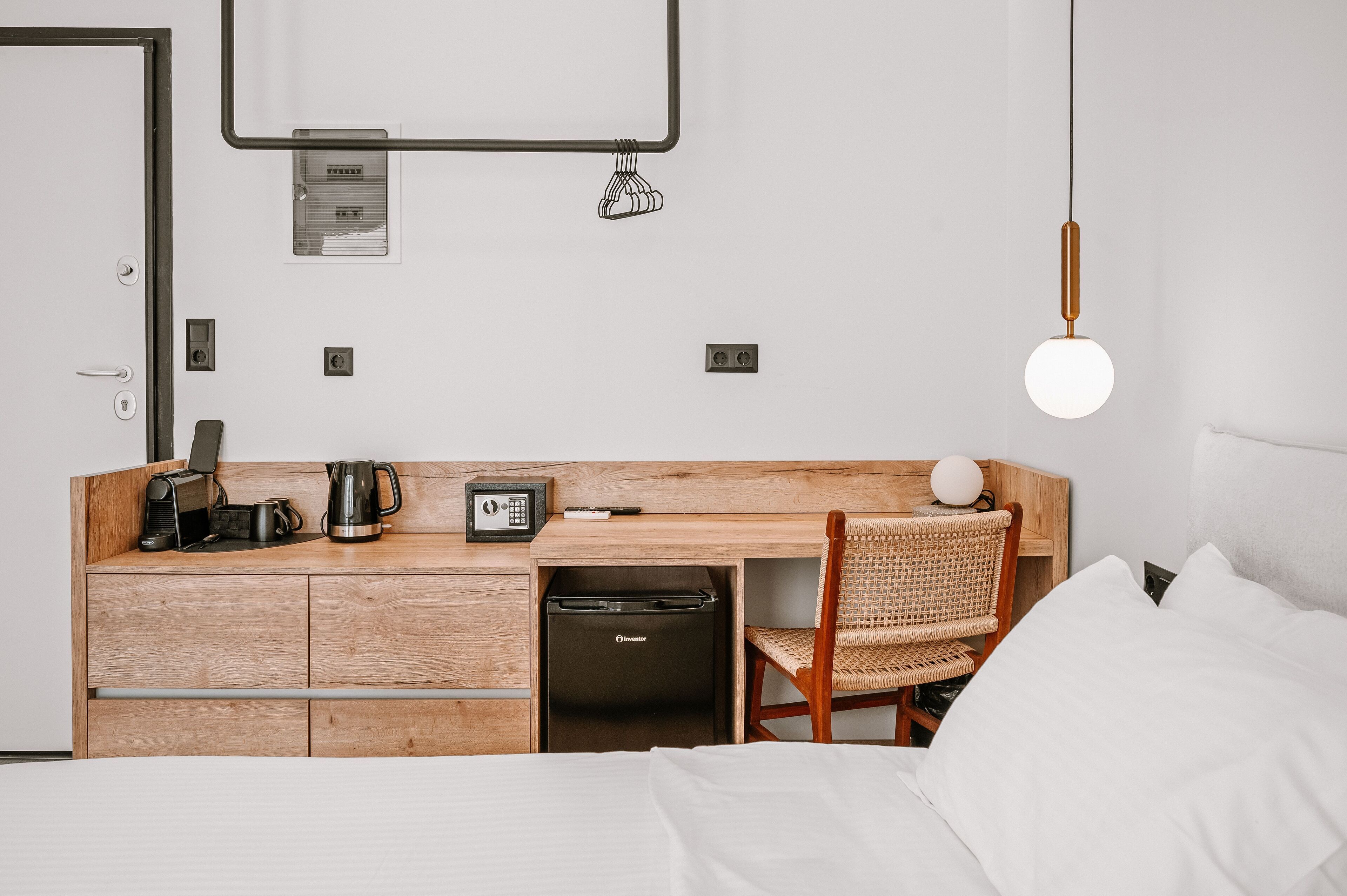 A hotel room with a wooden desk, a chair, a bed, and a hanging light fixture.